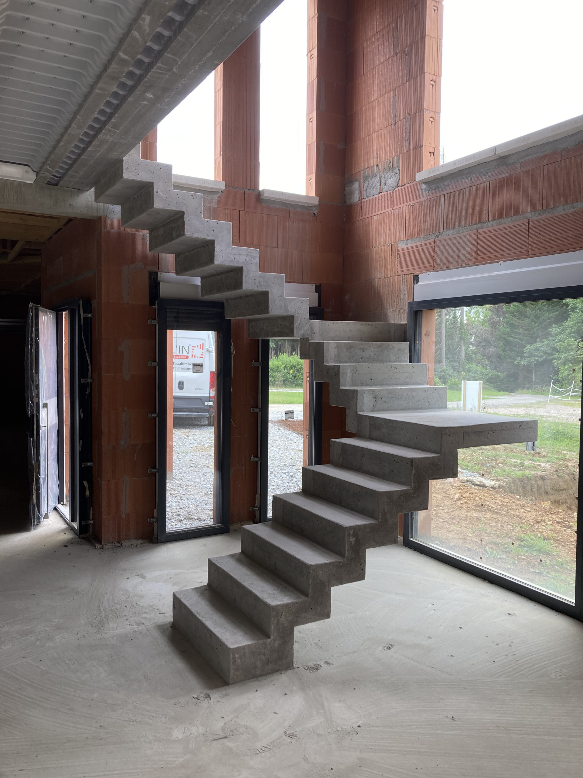 escalier béton à crémaillère devant une baie vitrée à châssis fixe.