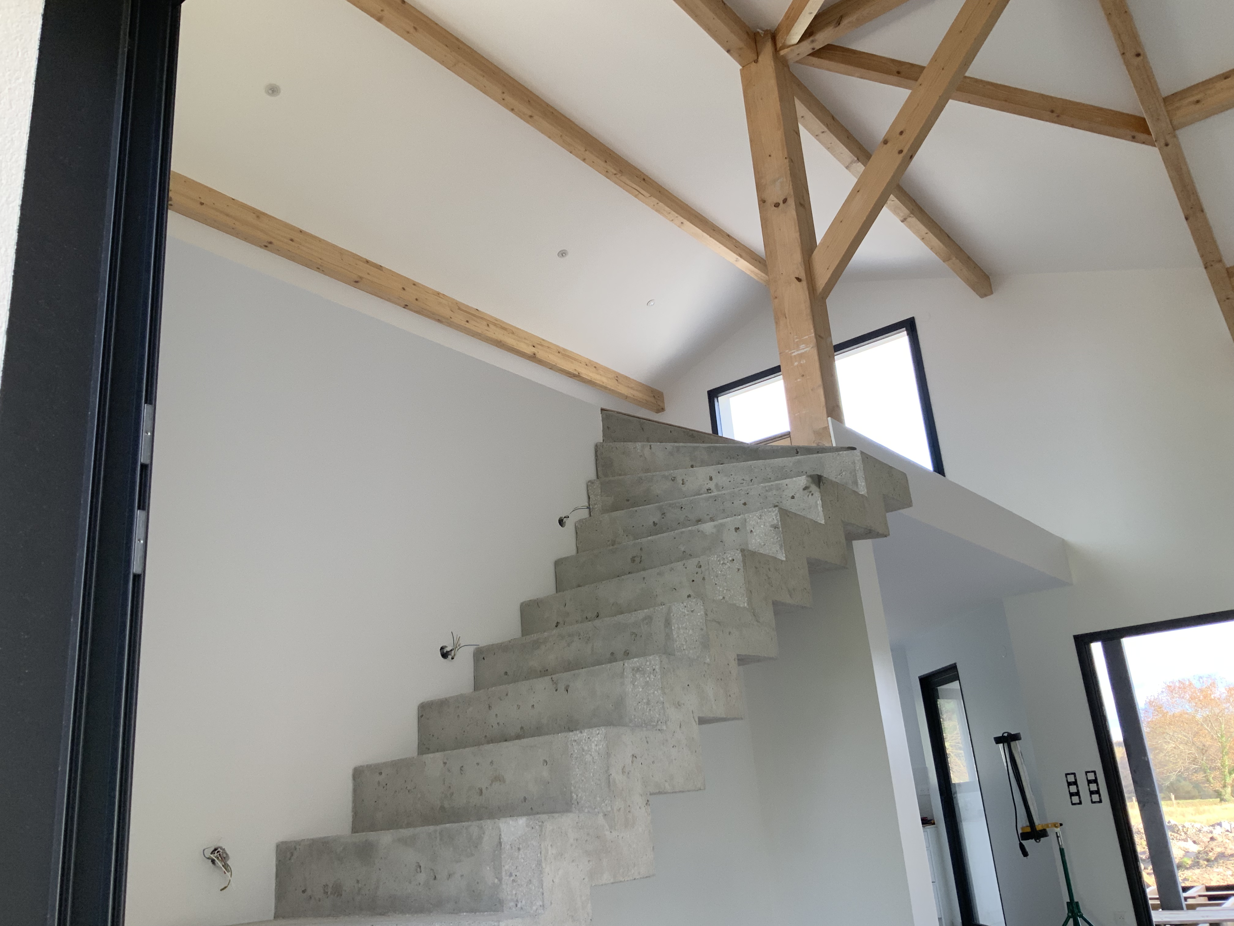 Escalier moderne à crémaillère donnant sur une mezzanine avec charpente apparente.